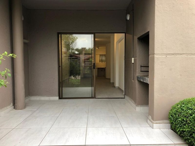 A covered patio featuring tiled flooring and a built-in braai, providing a seamless transition to the interior living space through a sliding glass door.