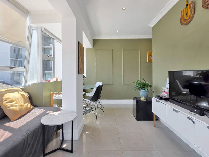 A bright living area featuring tiled flooring, decorative wall molding, recessed downlighting, and large windows that provide ample natural light.