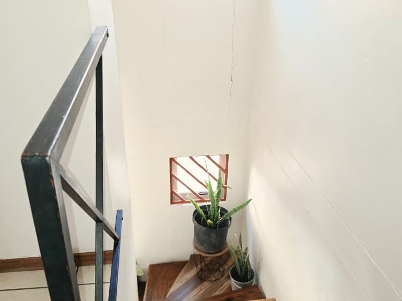 A staircase featuring timber treads and a metal handrail, with a visible vertical crack on the adjacent wall.