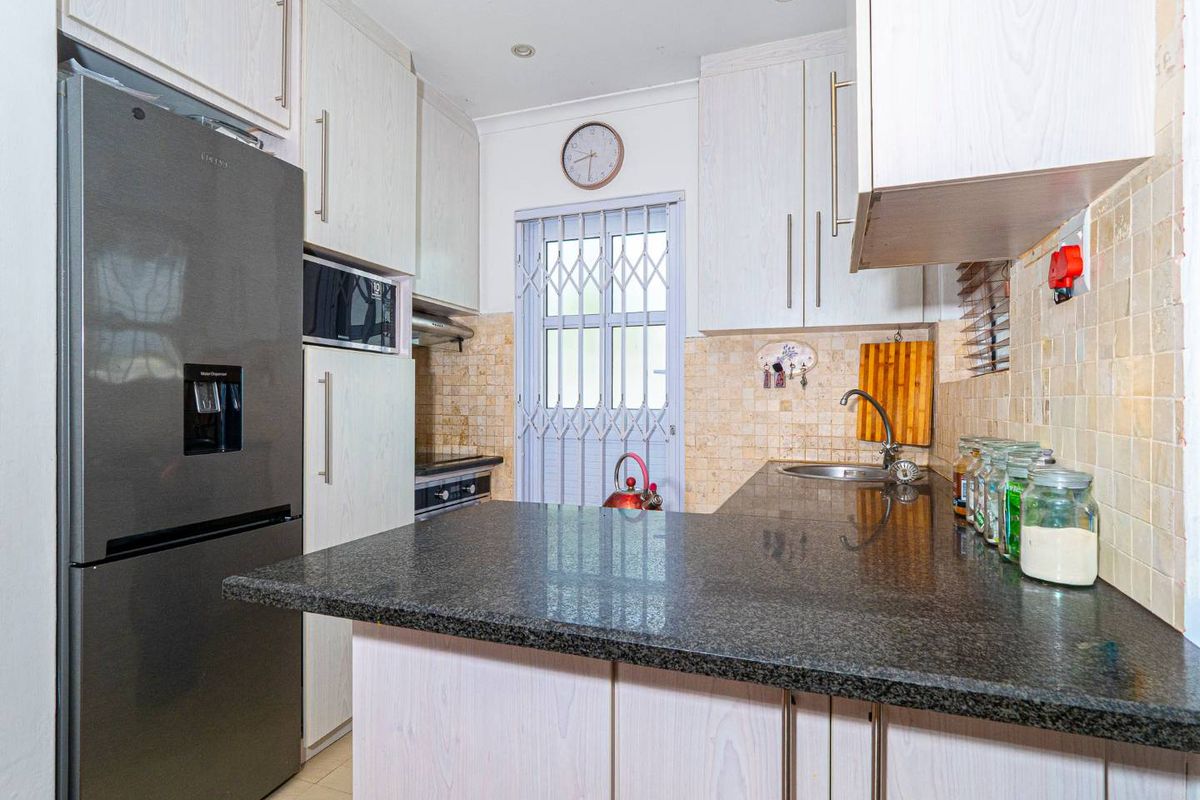 Compact kitchen featuring granite countertops, light wood-grain cabinetry, built-in oven, and a security gate leading to the exterior.