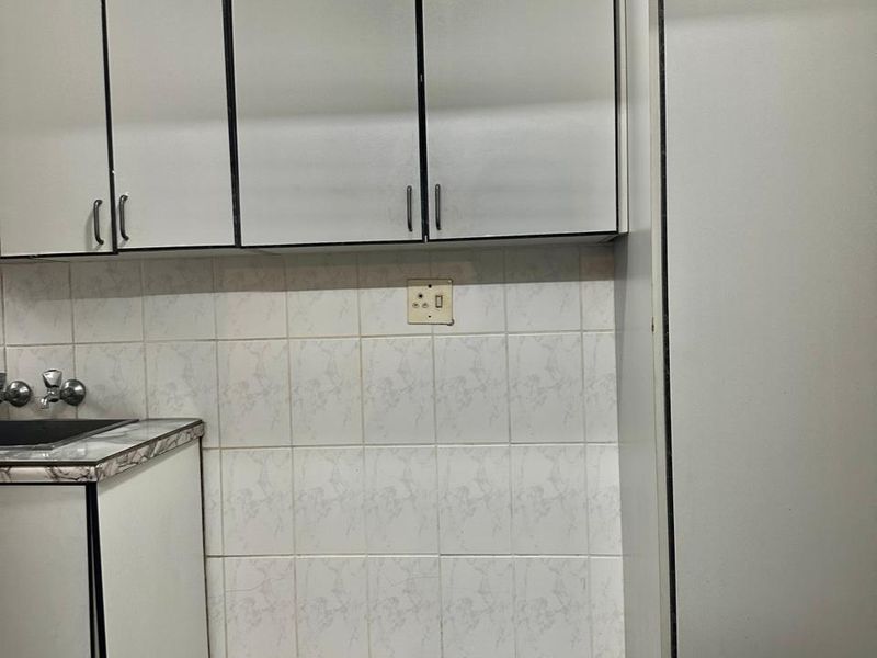 A functional kitchen area featuring white built-in cabinetry, a tiled backsplash, and dark floor tiles, offering a blank canvas for potential modernization.
