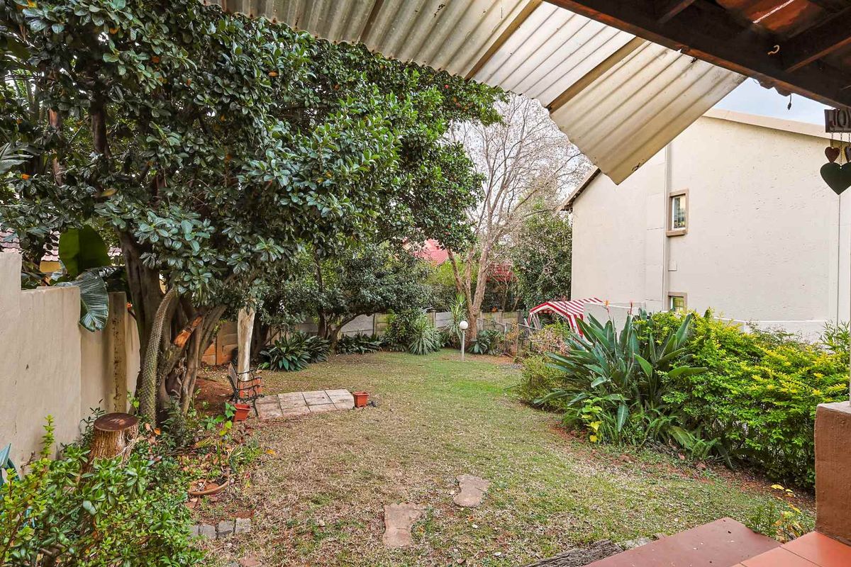 A private rear garden featuring a covered patio area, established trees, and a paved walkway leading through the lawn.