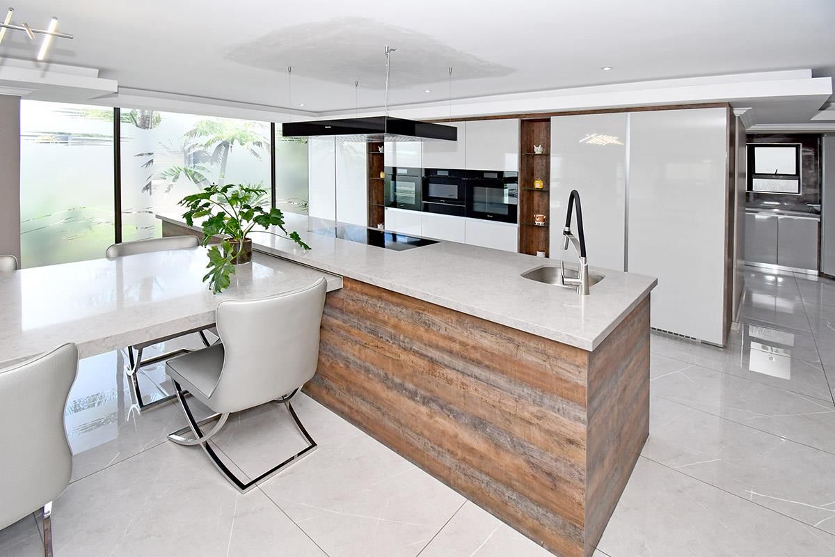 Modern open-plan kitchen featuring a large central island with stone countertops, integrated appliances, sleek cabinetry, and polished floor tiles.