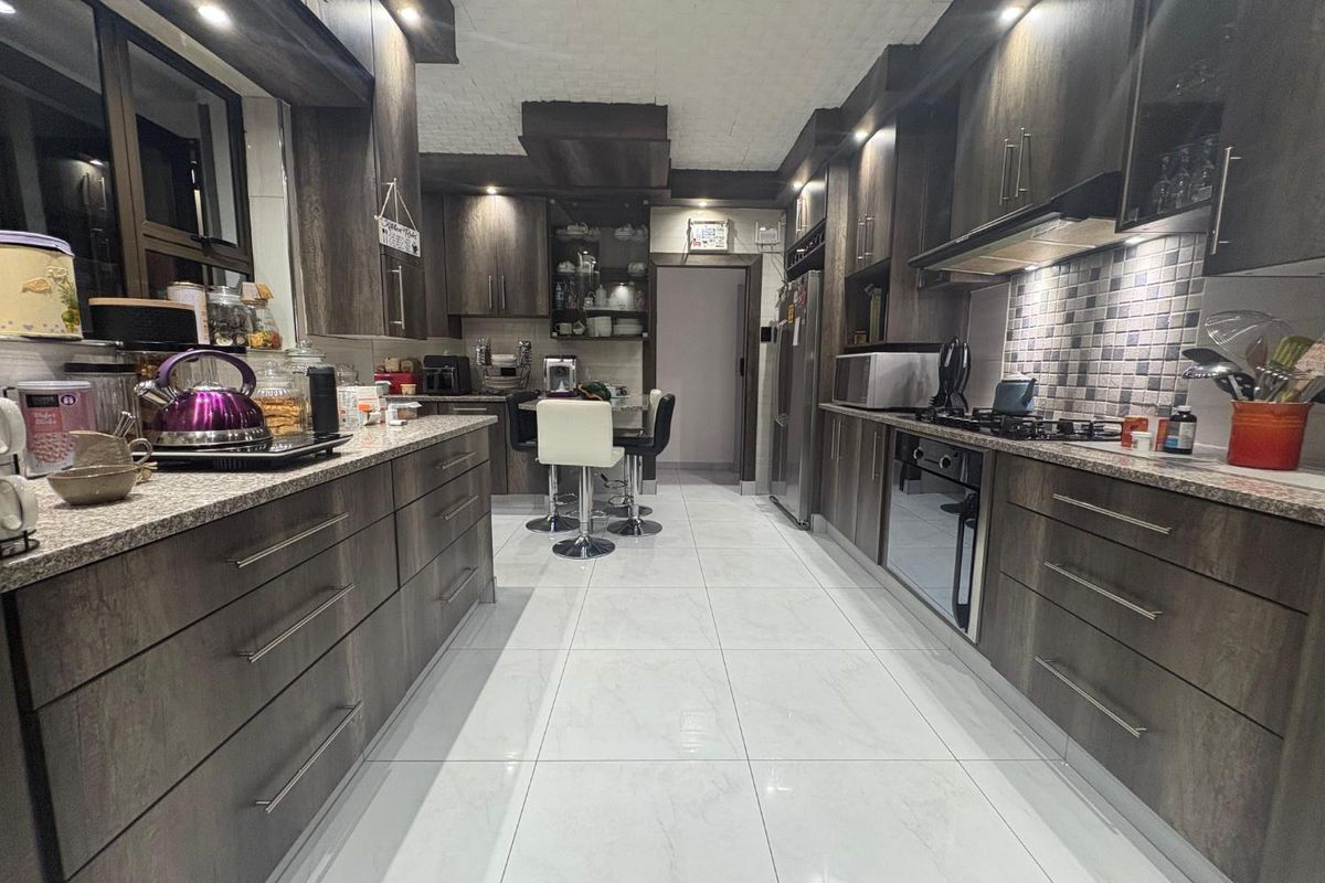Modern galley-style kitchen featuring dark wood cabinetry, granite countertops, a gas hob, built-in oven, and stylish mosaic tile backsplash with polished floor tiles.