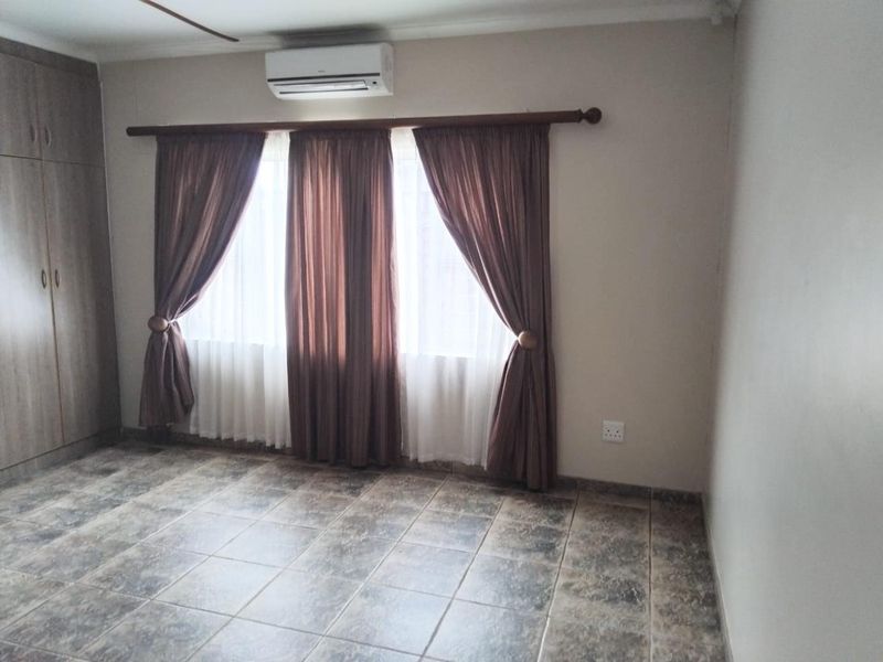 A spacious bedroom featuring tiled flooring, built-in cupboards, and a wall-mounted air conditioning unit.