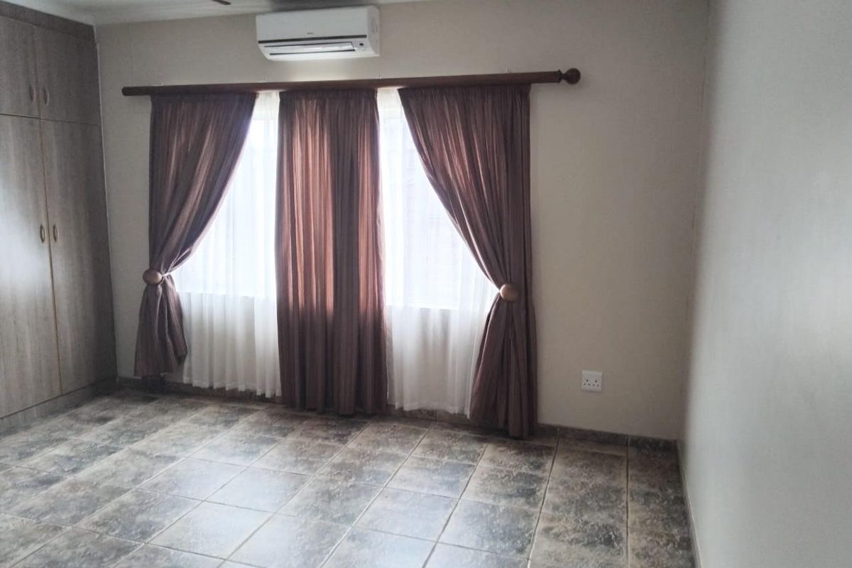 A spacious bedroom featuring tiled flooring, built-in cupboards, and a wall-mounted air conditioning unit.