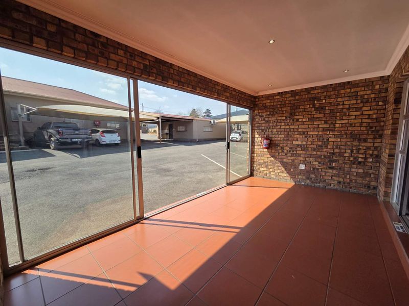 A spacious, empty covered patio featuring exposed brick walls, tiled flooring, and large sliding glass doors providing access to the exterior parking area.