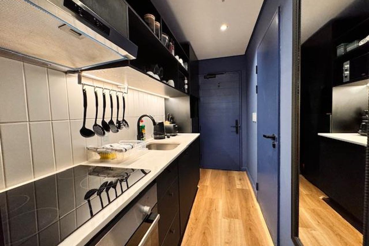A modern, compact galley kitchen featuring dark cabinetry, integrated appliances, a sleek induction hob, and light wood-look flooring.