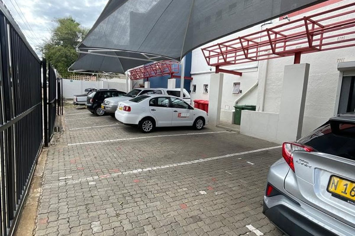 Outdoor paved parking area featuring a shade cloth canopy structure and secure metal perimeter fencing.