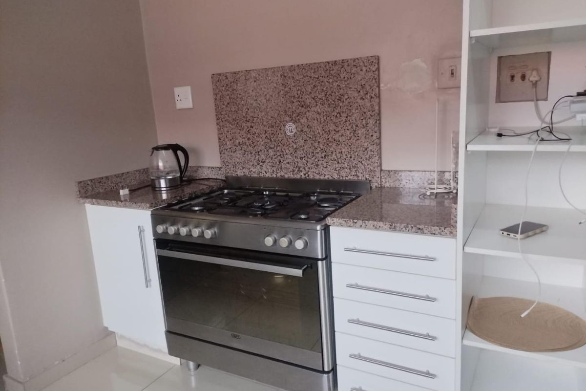 A compact kitchen featuring granite countertops, a gas stove with oven, and white cabinetry with tiled flooring.