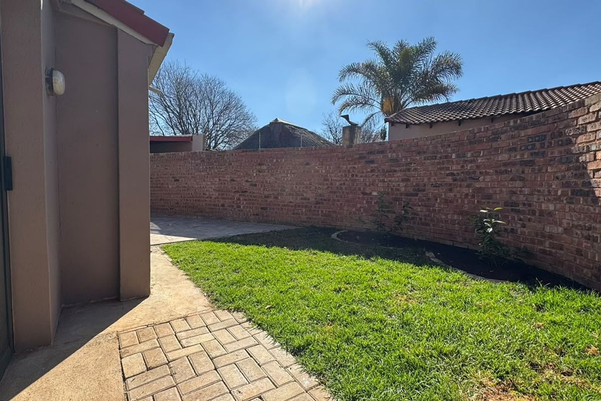 A private rear garden featuring a well-maintained lawn, paved walkway, and a secure brick boundary wall, accessible via a sliding glass door.