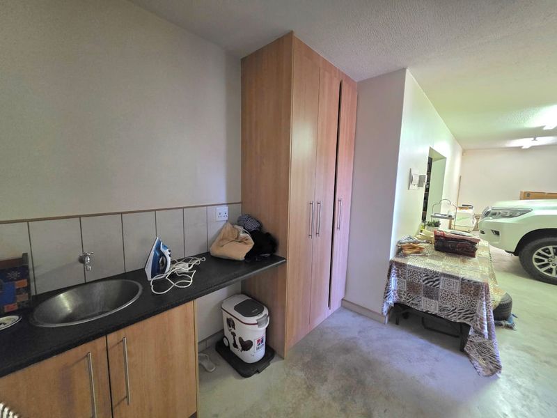 A functional laundry area featuring built-in cabinetry, a stainless steel sink, and a tiled splashback, conveniently located adjacent to the garage space.
