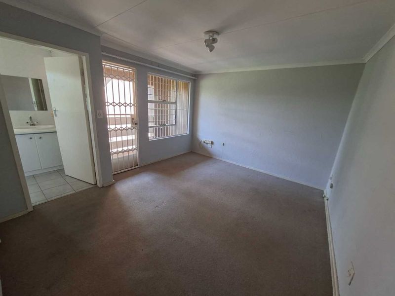 An empty bedroom featuring carpeted flooring, security gate access, and an adjoining bathroom, offering a blank canvas for renovation or staging.