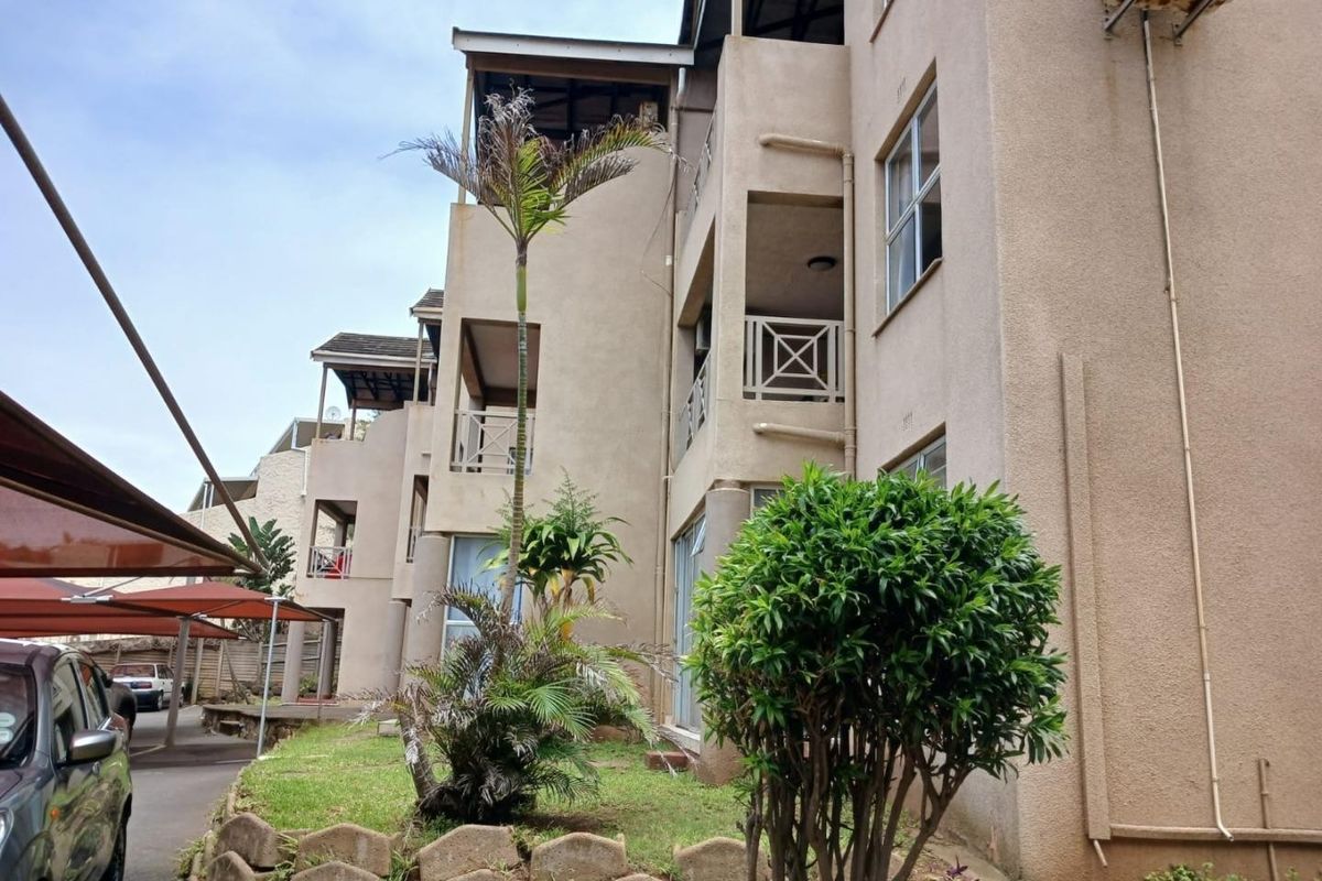 Exterior view of an apartment complex featuring multiple balconies, landscaped garden areas, and covered parking bays.