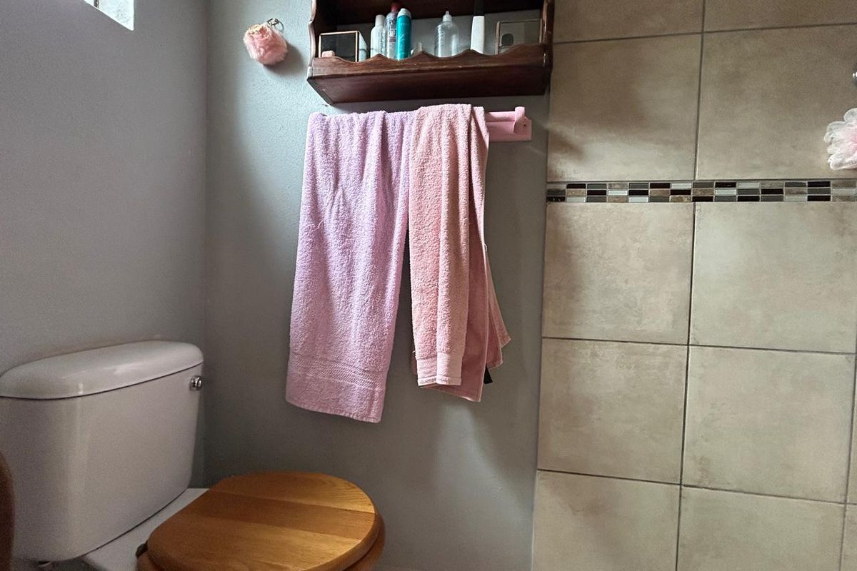 A functional bathroom featuring a standard toilet, tiled shower wall with decorative mosaic inlay, and wall-mounted storage shelving.