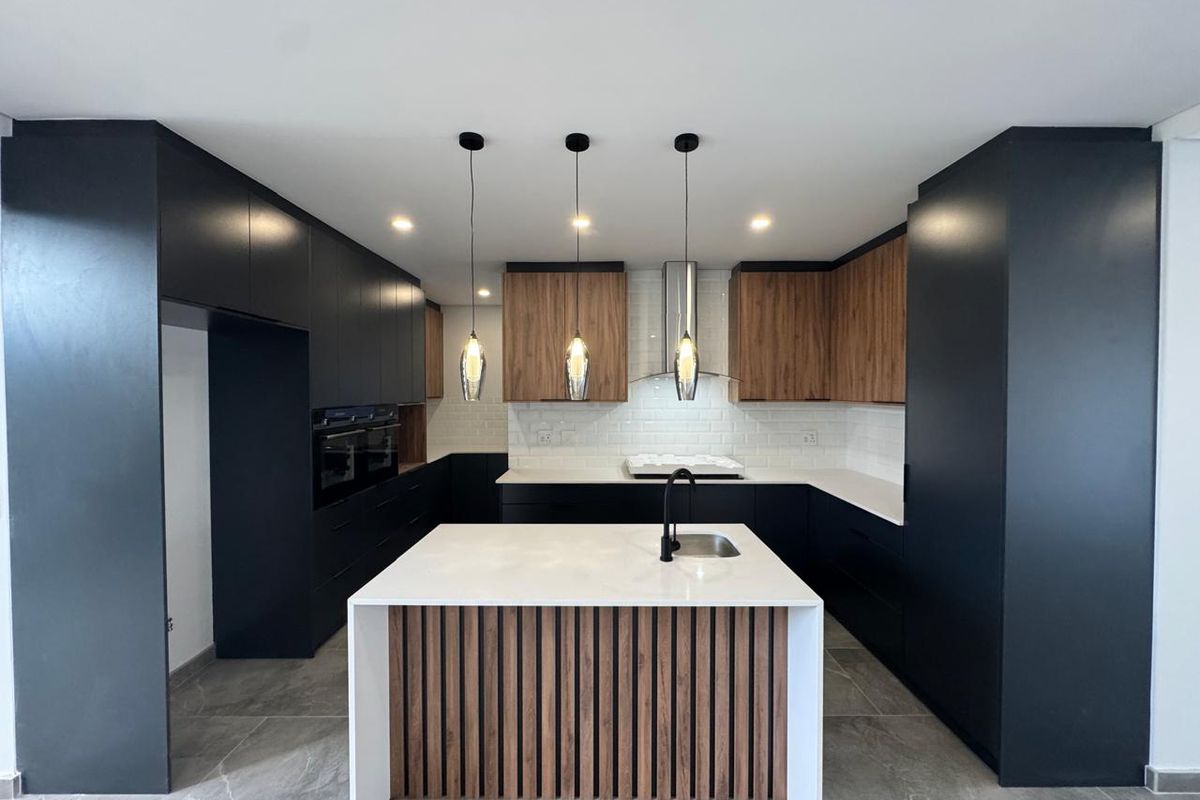 Modern kitchen featuring sleek black and wood-tone cabinetry, a central island with stone countertop, integrated appliances, and stylish pendant lighting.