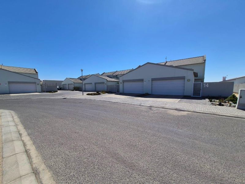 A street-level view of a townhouse complex featuring multiple units with paved driveways, garage doors, and tiled roofing under a clear sky.