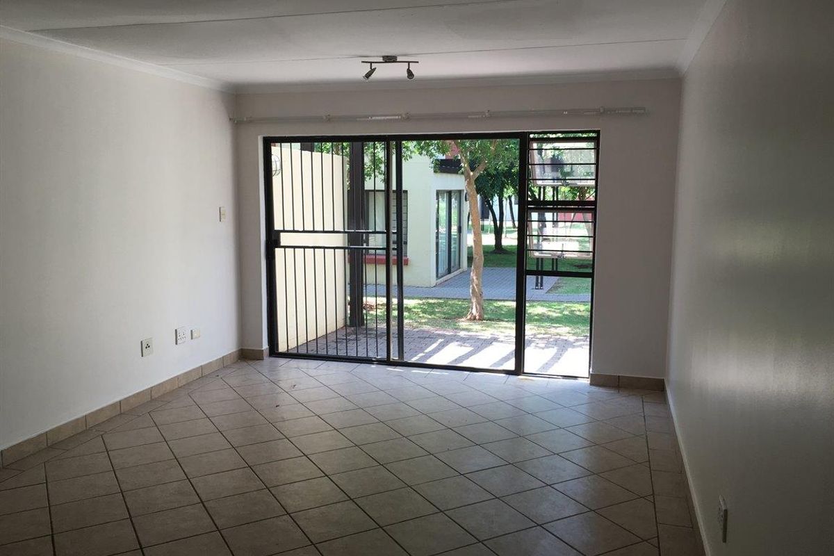 An empty living room featuring tiled flooring, a sliding glass door with a security gate, and access to an outdoor area.