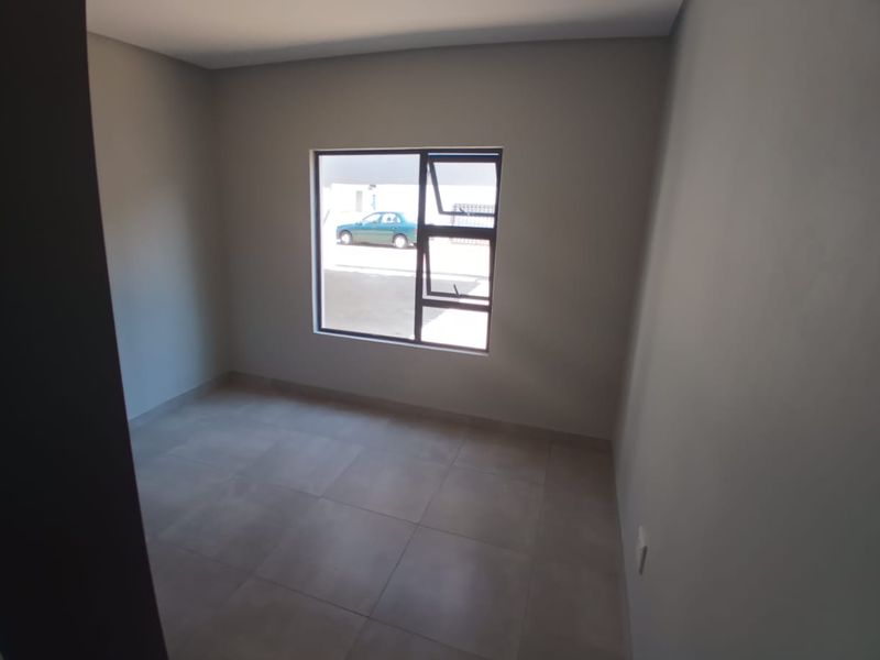 A clean, empty bedroom featuring neutral grey tiled flooring and a modern aluminium window frame, providing a blank canvas for interior design.