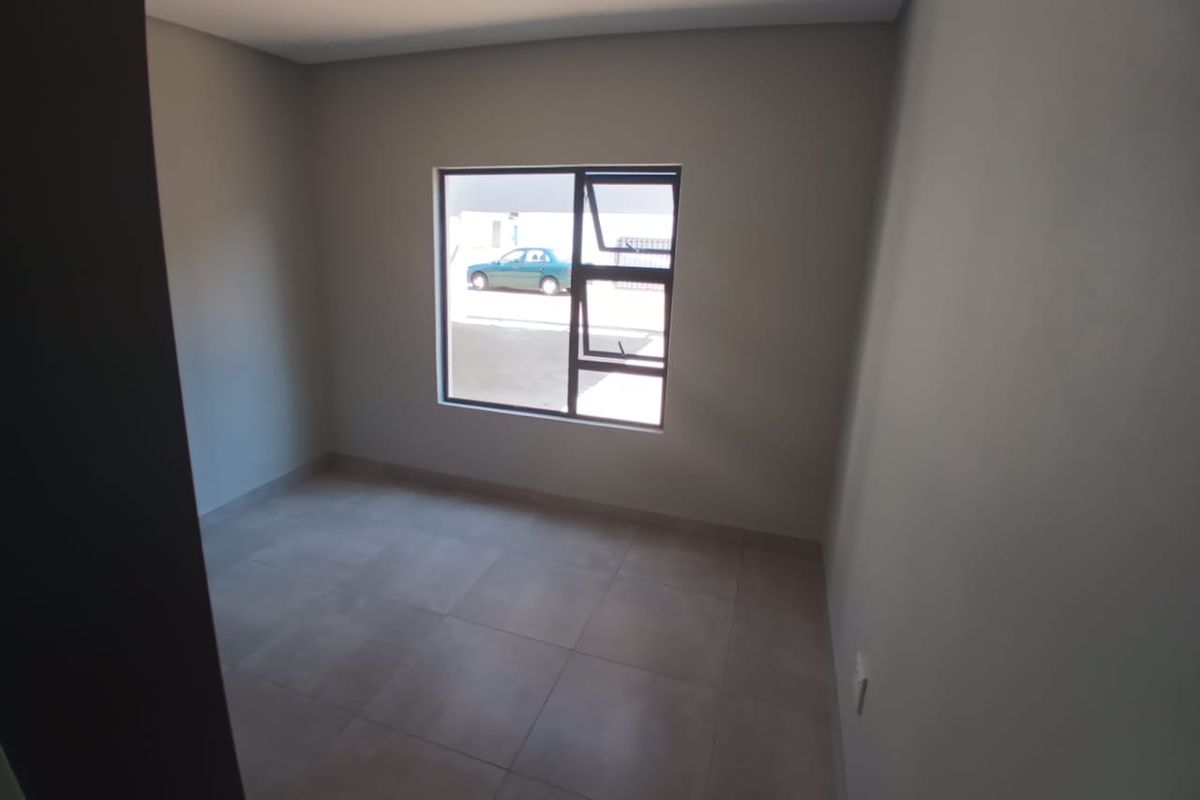 A clean, empty bedroom featuring neutral grey tiled flooring and a modern aluminium window frame, providing a blank canvas for interior design.