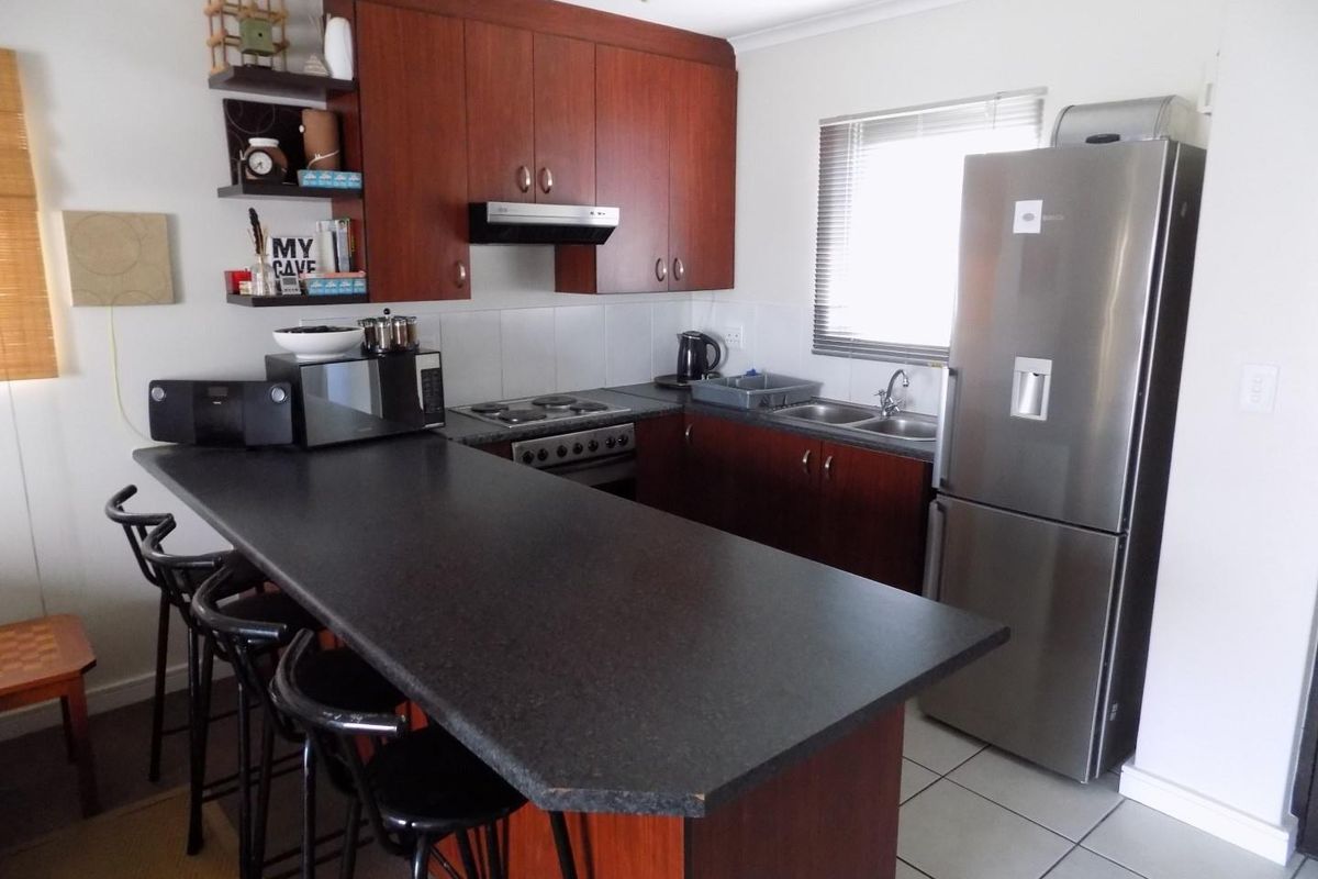 Compact kitchen featuring dark wood-look cabinetry, laminate countertops with an integrated breakfast bar, and tiled flooring.