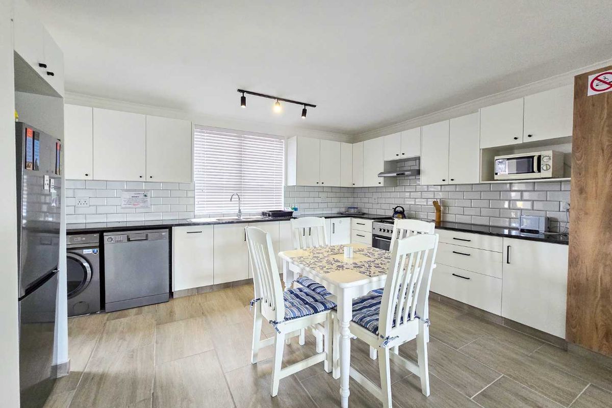 A bright, functional kitchen featuring white cabinetry, subway tile backsplash, dark countertops, and integrated space for laundry appliances.