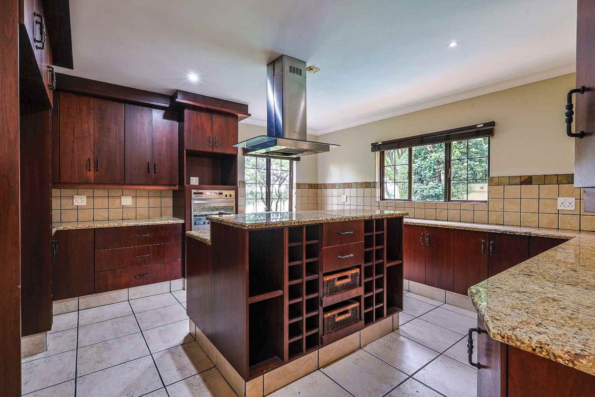 Spacious kitchen featuring dark wood cabinetry, granite countertops, a central island with built-in wine storage, and a stainless steel extractor fan.