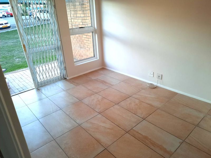 An empty living area featuring neutral tiled flooring, a large window, and a secure metal entrance gate leading to the exterior.