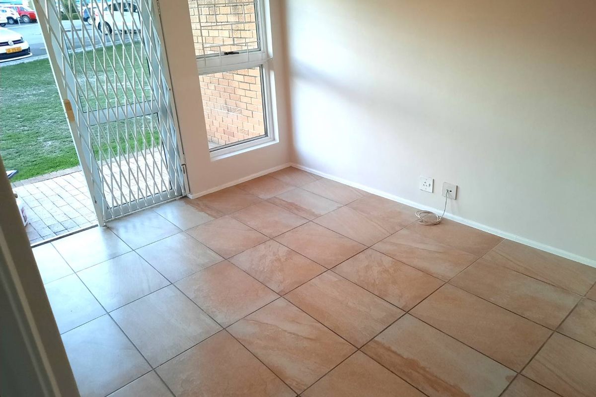 An empty living area featuring neutral tiled flooring, a large window, and a secure metal entrance gate leading to the exterior.