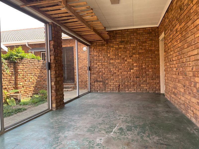 A covered patio area featuring exposed brick walls, a wooden pergola, and sliding glass doors leading to the garden.