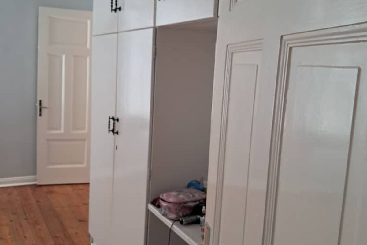 A bedroom featuring original timber flooring, built-in white cabinetry with overhead storage, and a classic panelled interior door.