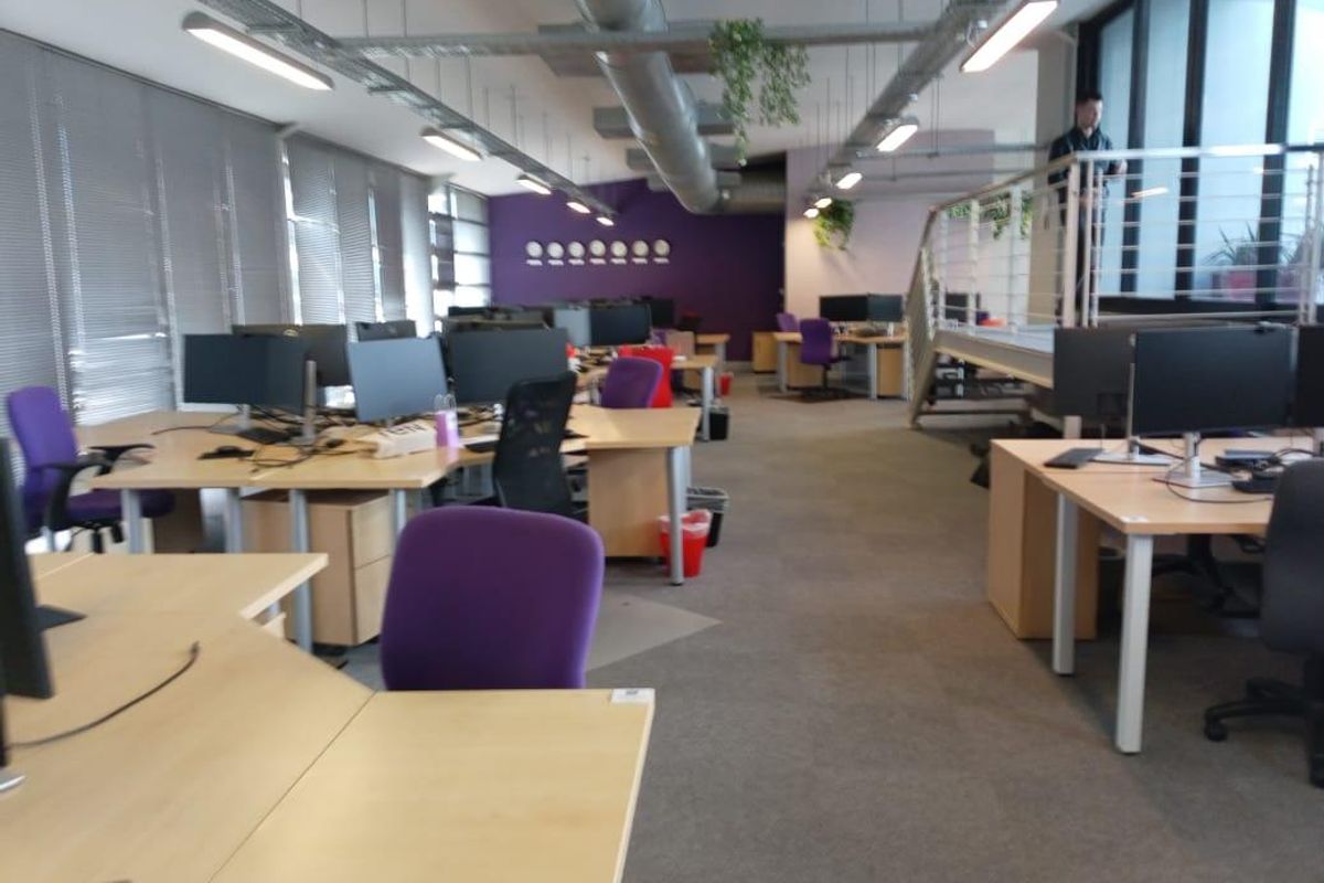 Open-plan office space featuring exposed industrial ductwork, linear lighting, and a mezzanine level with a metal staircase.