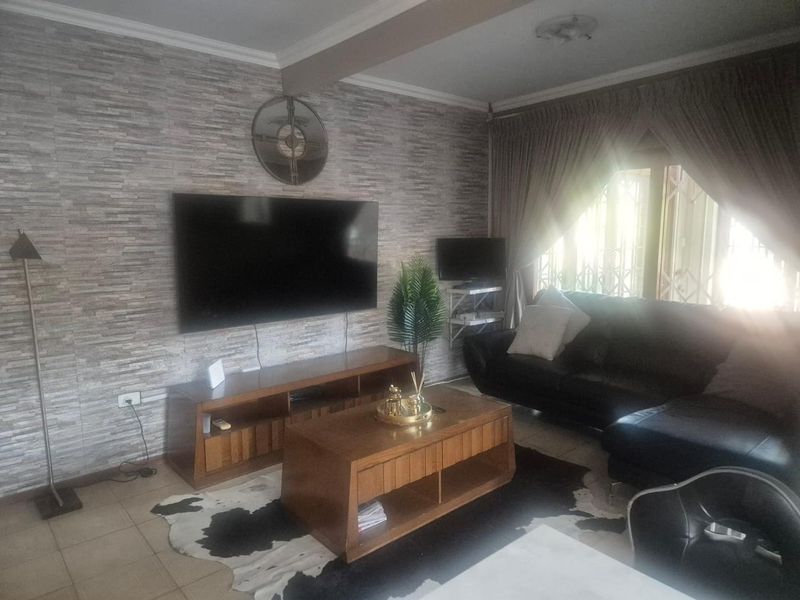 A living room featuring a textured stone-cladding accent wall, tiled flooring, and natural light entering through a window with security gate.