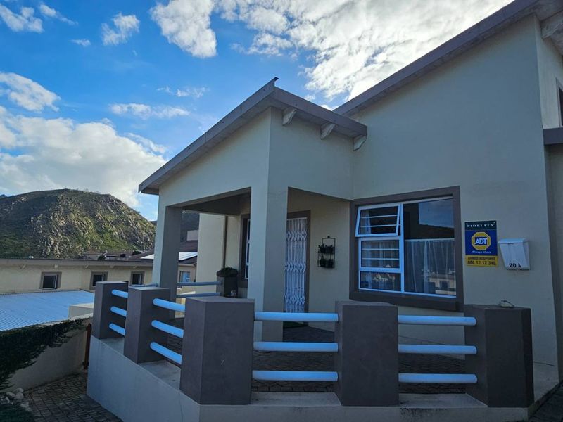 Front elevation of the cluster home featuring a covered patio, masonry balustrade, and an integrated garage with mountain views in the background.