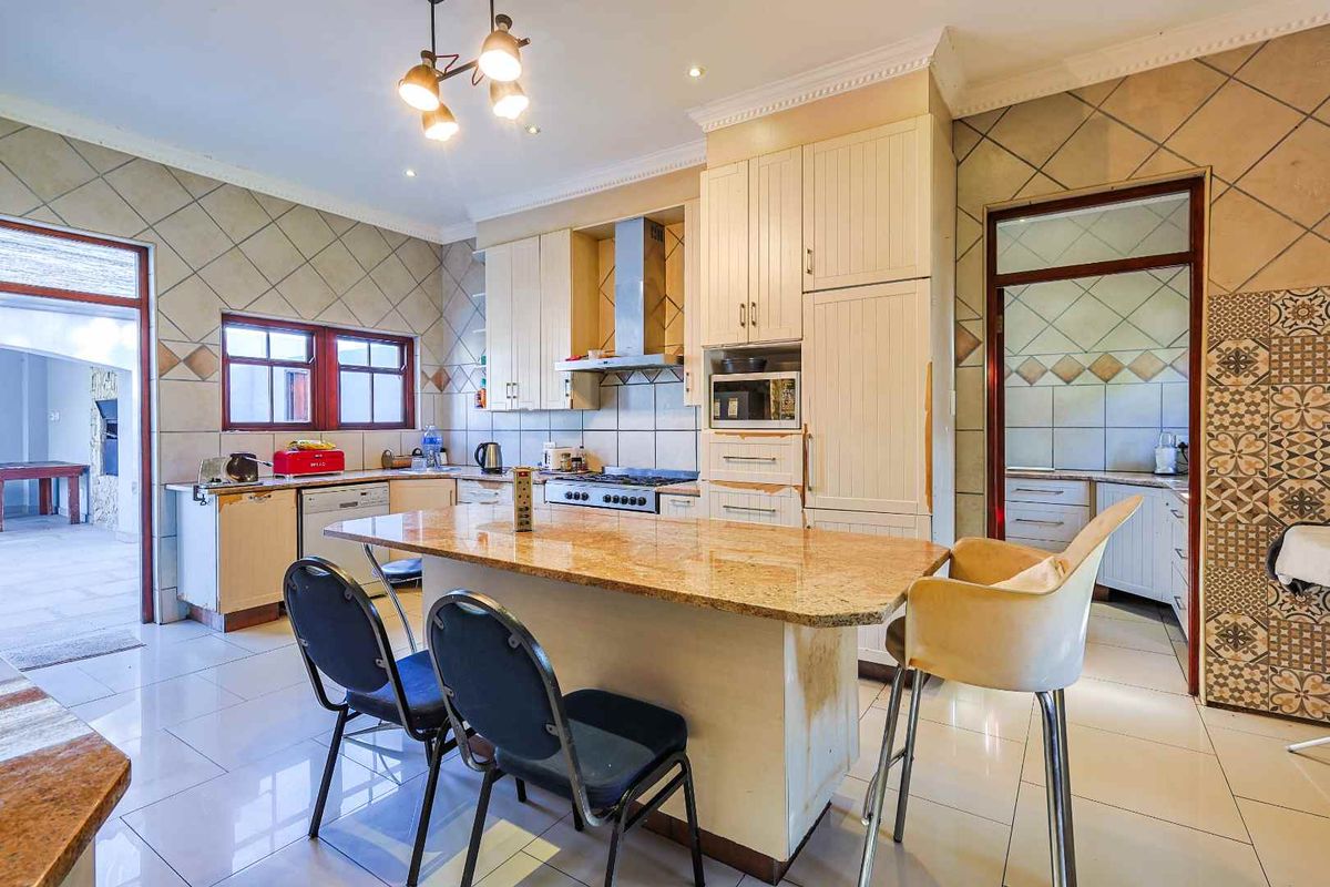 Spacious kitchen featuring a central island with granite countertop, built-in cabinetry, stainless steel extractor fan, and tiled flooring throughout.