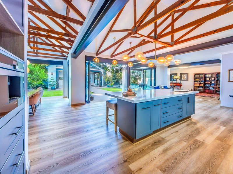 Spacious open-plan living area featuring exposed timber trusses, a modern kitchen island with stone countertops, and seamless indoor-outdoor flow through large bi-fold doors.