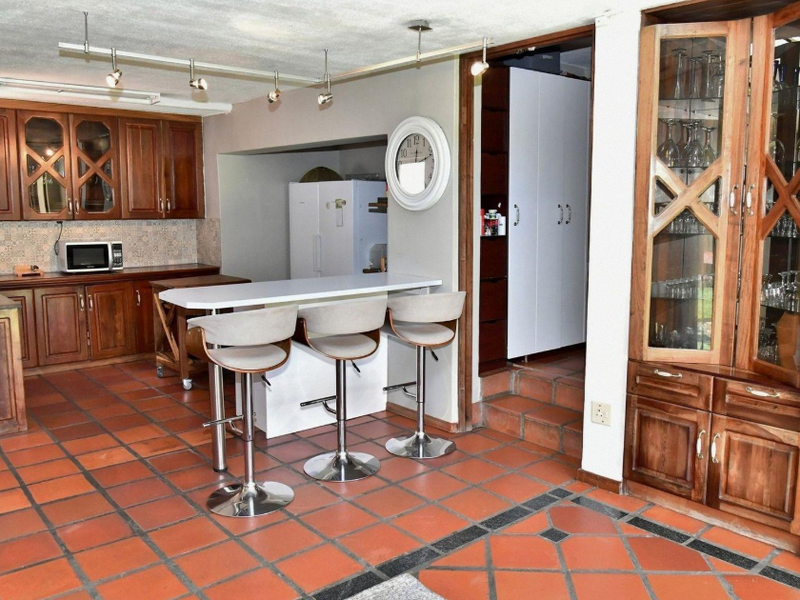 A traditional kitchen featuring wooden cabinetry, a central breakfast bar, and terracotta-style tiled flooring with integrated display storage.