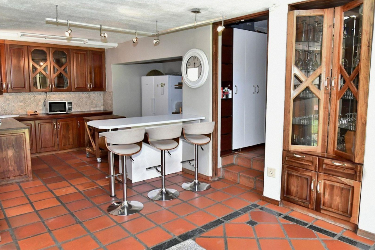 A traditional kitchen featuring wooden cabinetry, a central breakfast bar, and terracotta-style tiled flooring with integrated display storage.