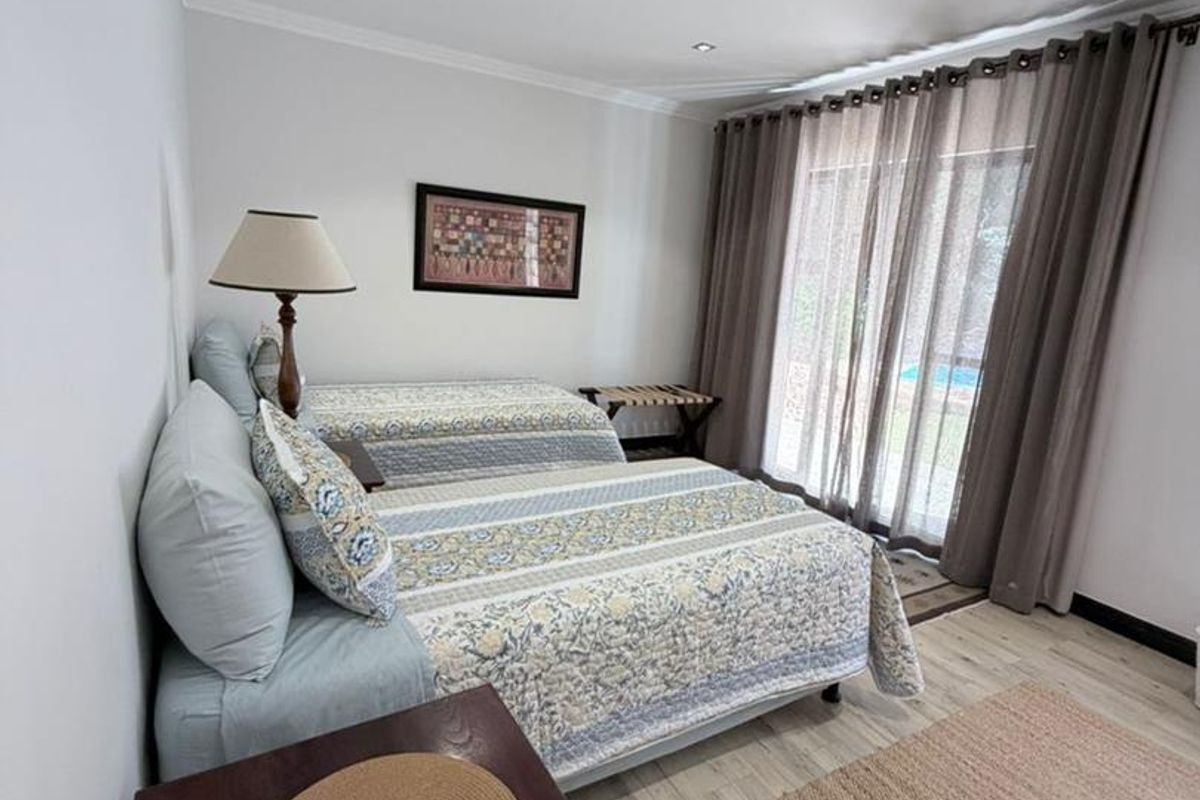 A bright bedroom featuring light-toned wood-look flooring, recessed ceiling lighting, and sliding glass doors providing direct access to the outdoor area.