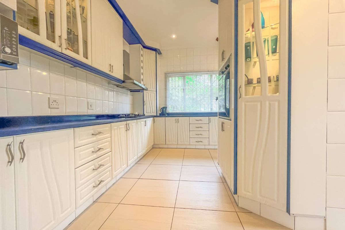 A galley-style kitchen featuring white cabinetry with blue trim, tiled flooring, built-in oven, and an extractor fan.