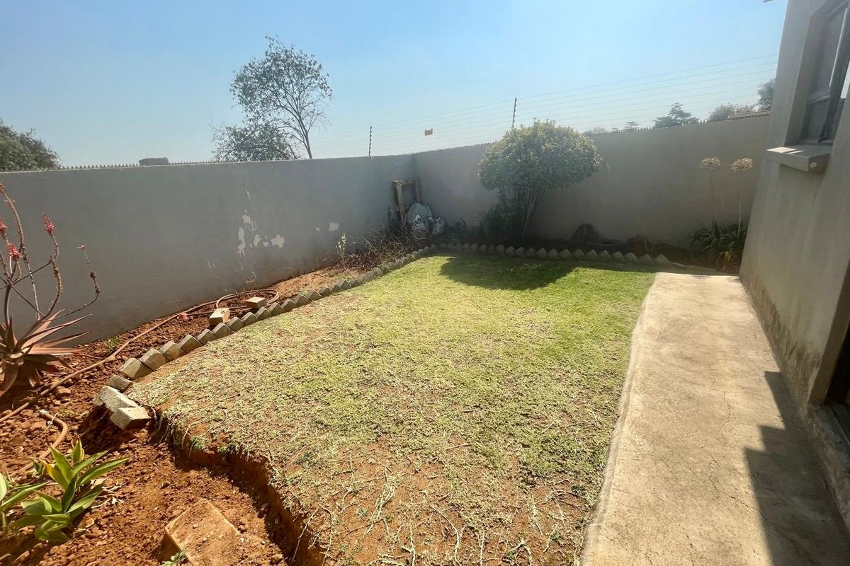 A compact rear garden area featuring a concrete walkway, perimeter wall with electric fencing, and a lawn area requiring maintenance.