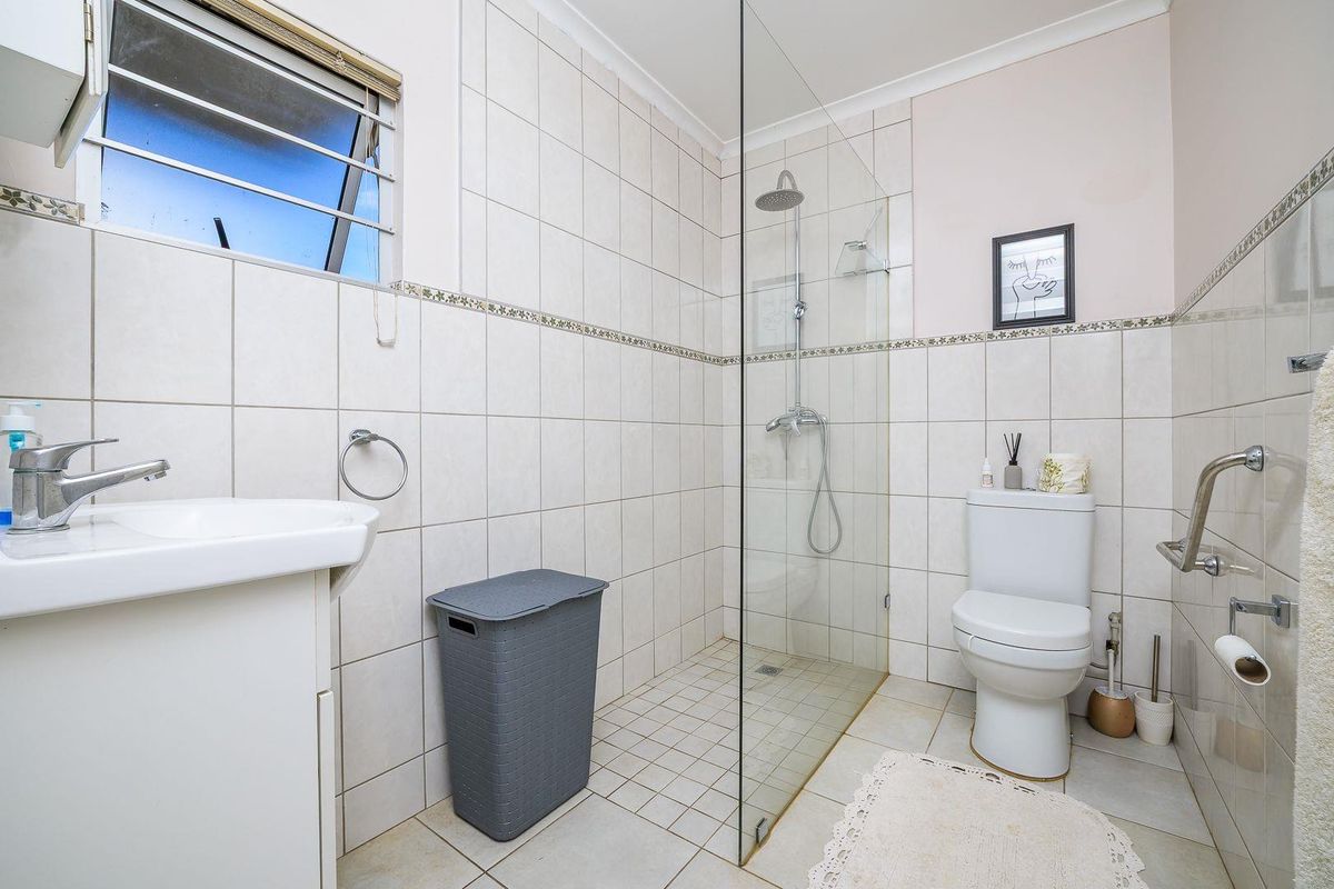 A functional bathroom featuring a walk-in glass shower, wall-mounted basin, and toilet with tiled walls and flooring.