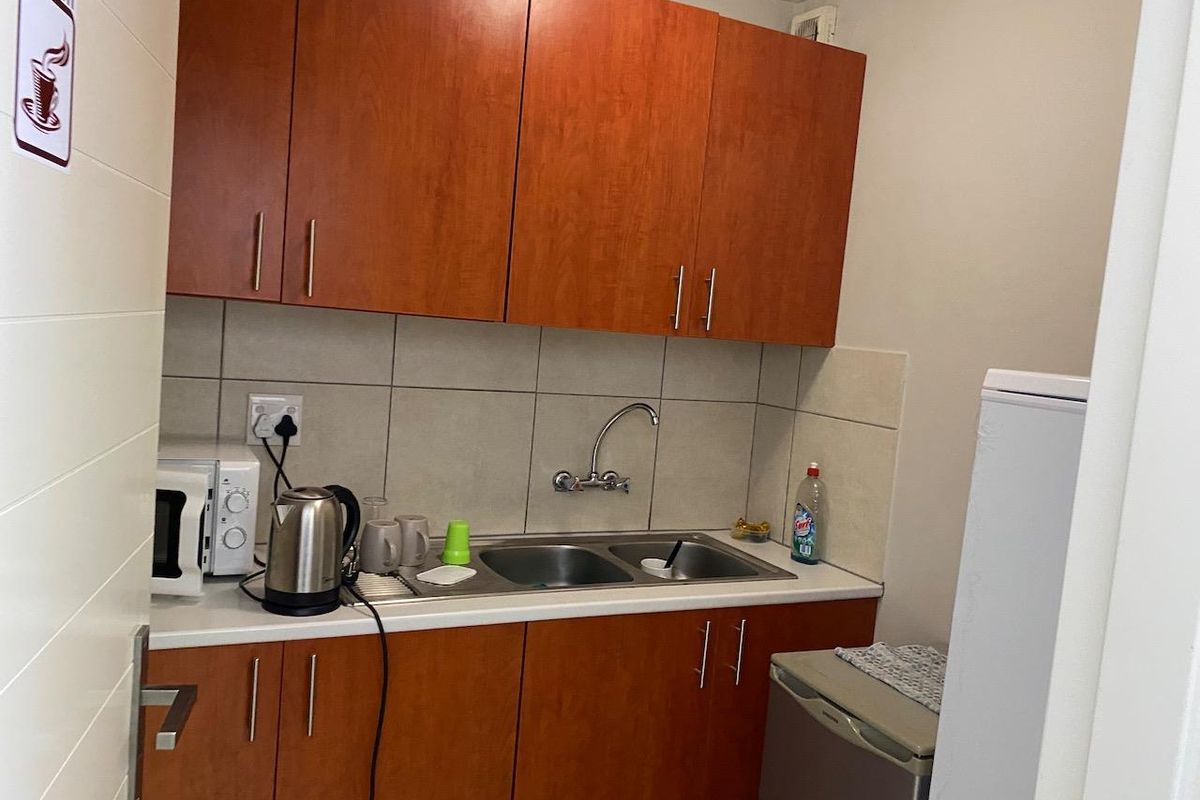 A compact kitchen area featuring wood-finish cabinetry, a double bowl stainless steel sink, and a tiled backsplash.