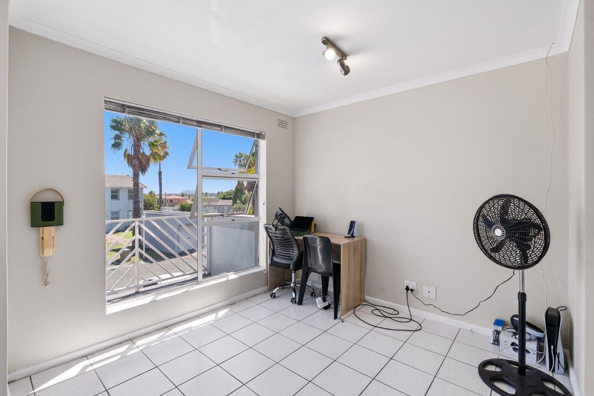 A bright bedroom featuring tiled flooring, a large window with exterior views, and a wall-mounted intercom system.