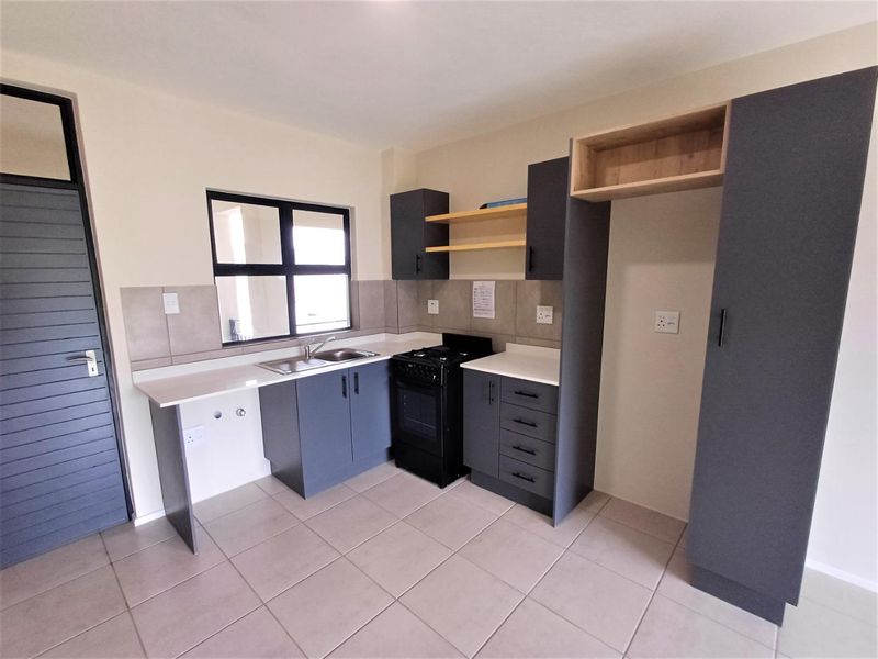 A modern, clean kitchen featuring dark grey cabinetry, light countertops, a built-in stove and oven, and neutral tiled flooring.