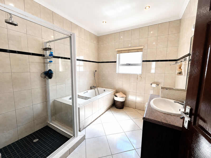 A well-maintained bathroom featuring a separate shower enclosure, a built-in bathtub, and a vanity unit with a basin, finished with neutral wall and floor tiles.