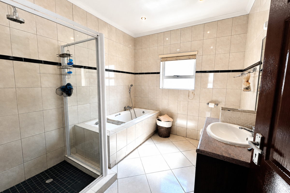 A well-maintained bathroom featuring a separate shower enclosure, a built-in bathtub, and a vanity unit with a basin, finished with neutral wall and floor tiles.
