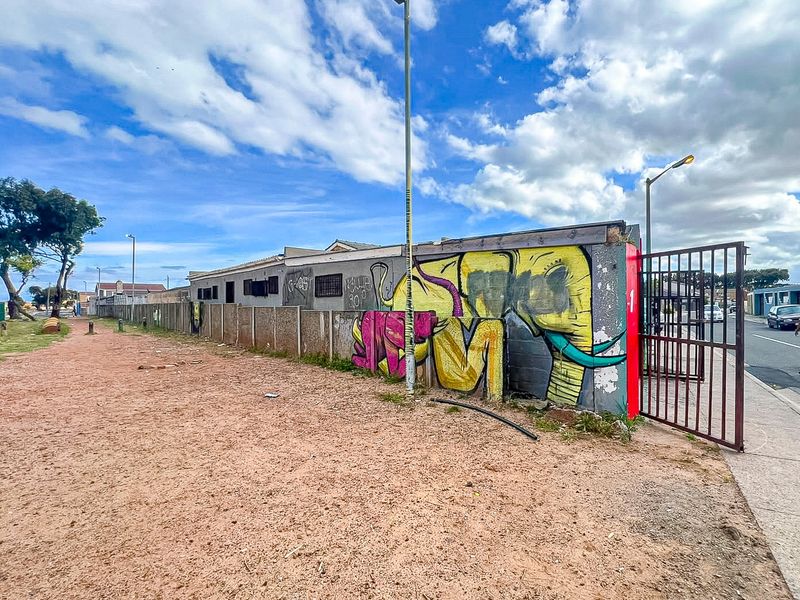 Rear exterior view of the property featuring a perimeter wall with graffiti, a metal gate, and an unpaved ground area.