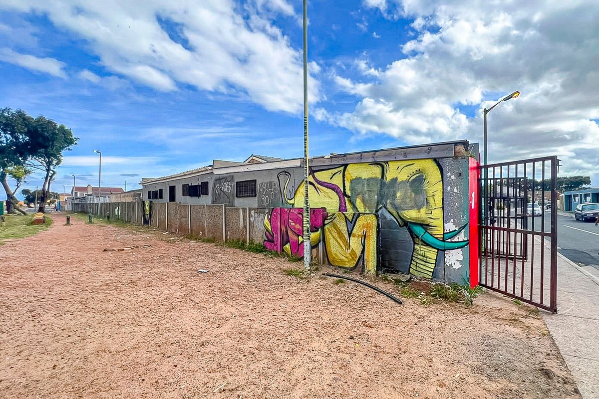 Rear exterior view of the property featuring a perimeter wall with graffiti, a metal gate, and an unpaved ground area.