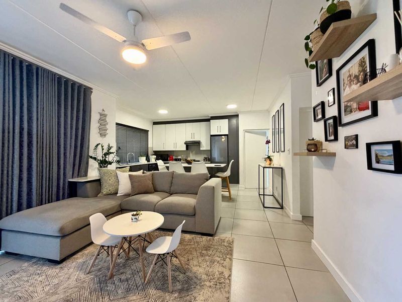 A bright open-plan living and kitchen area featuring modern cabinetry, a central island, tiled flooring, and a ceiling fan.